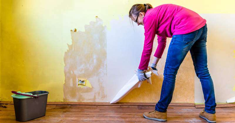 woman removing old paint from the wall
