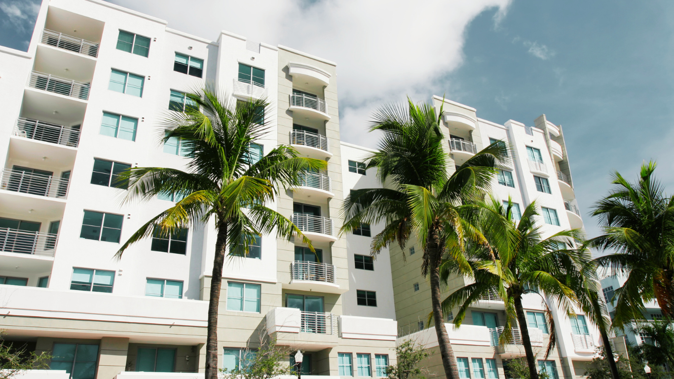 Modern beachfront condos in Naples, Florida, with palm trees and balconies under a sunny sky—ideal for anyone considering buying beach condos in Naples Florida.